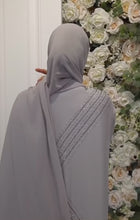 Back view of a grey abaya and khimar set featuring crystal embellishments, worn by a model in front of a floral background